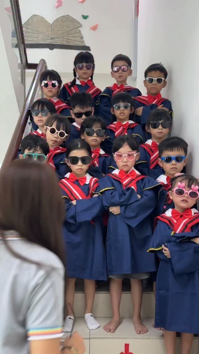 Young children in blue graduation gowns and sunglasses posing on a white staircase.