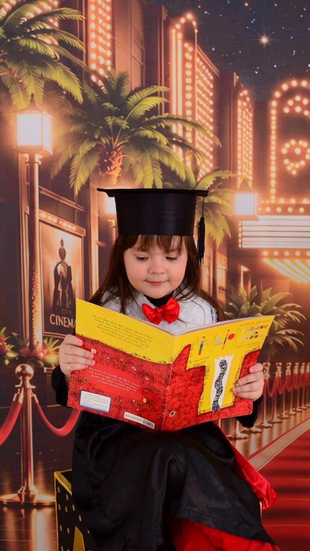 Young girl in graduation cap and gown reading a book before Hollywood backdrop