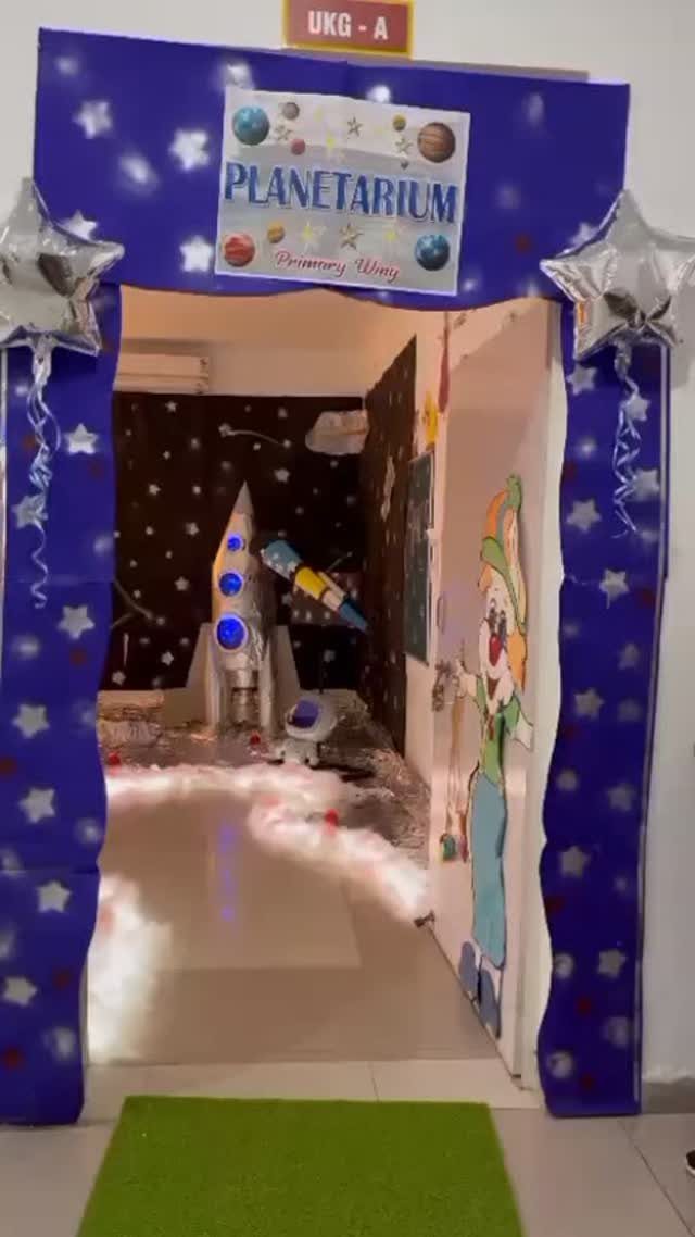 Space themed doorway decoration with a planetarium sign, rocket ship, and star balloons.