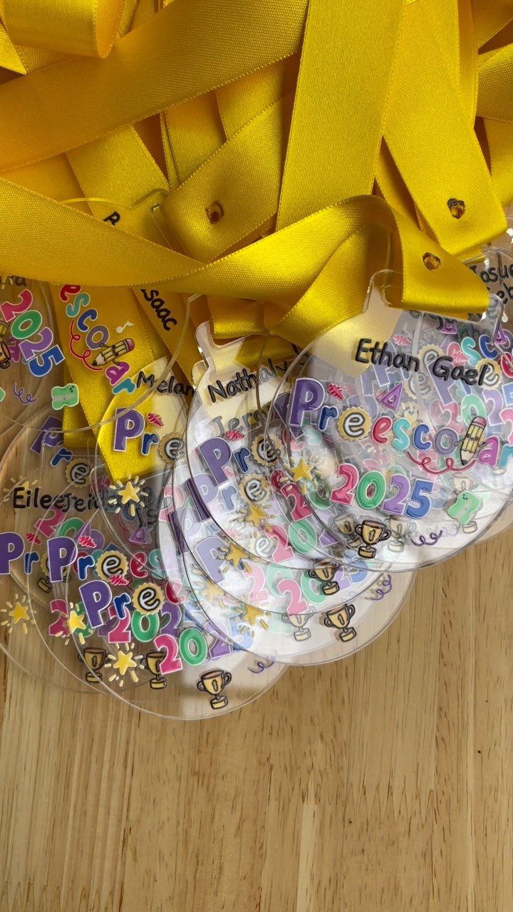 Personalized acrylic preschool graduation medals with yellow ribbons on a wooden table