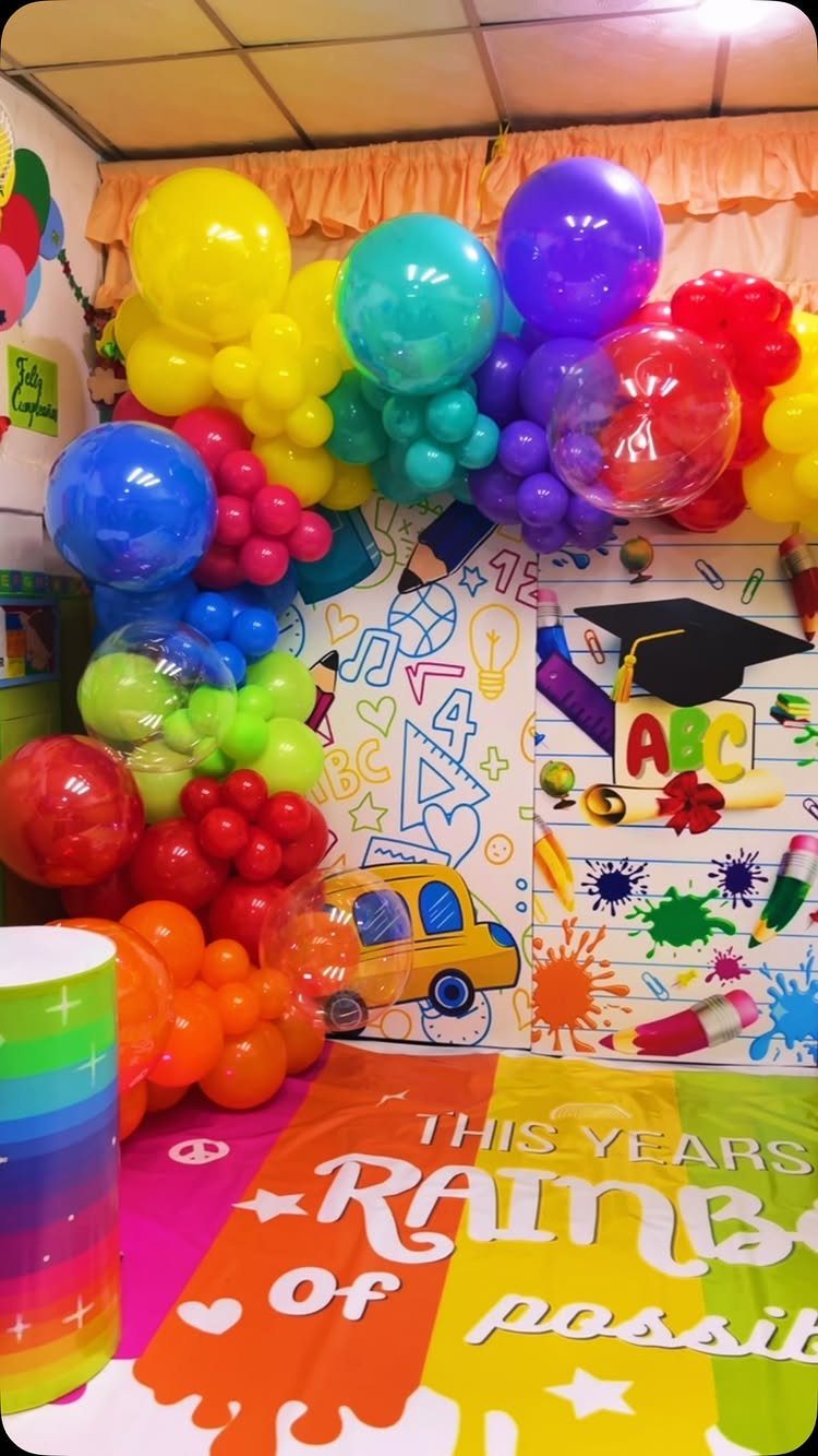 Rainbow balloon arch and school-themed backdrop for a preschool graduation celebration.