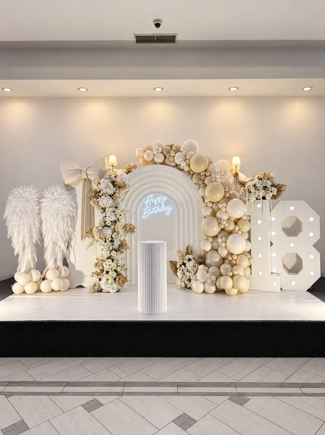 White birthday party setup with balloons, flowers, and a large glowing number 18.