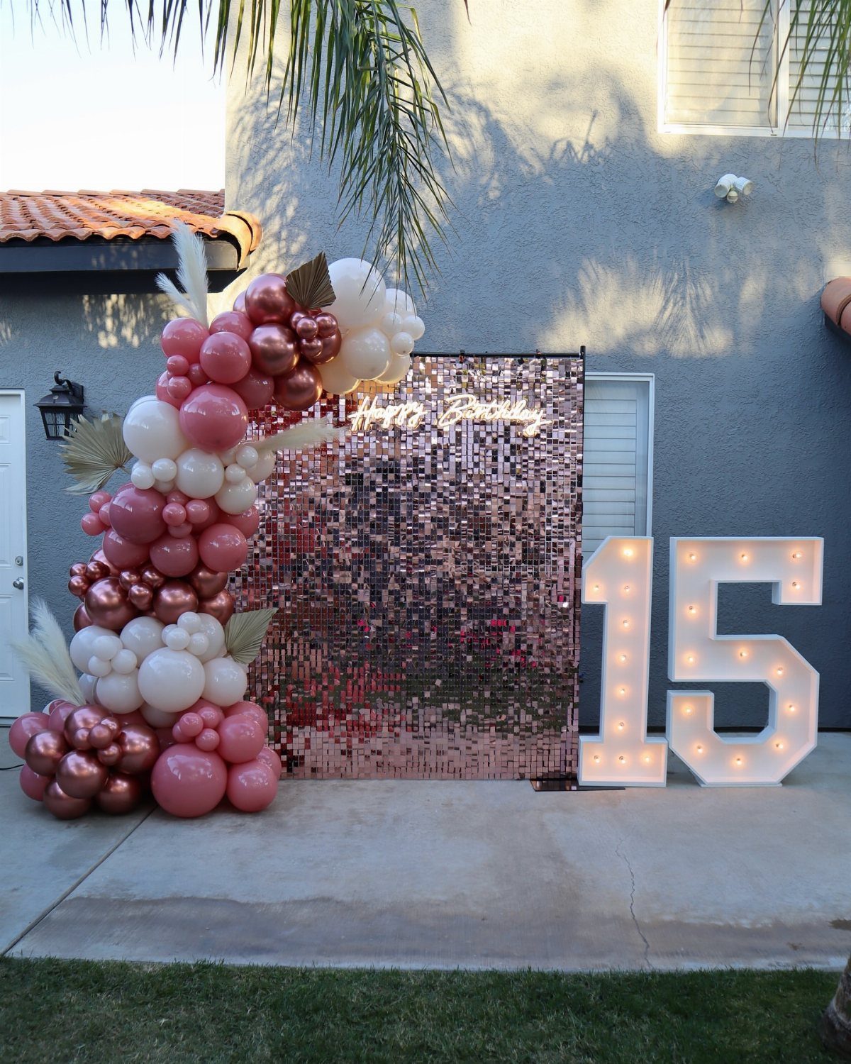 Rose gold sequin backdrop with pink and white balloon arch and lit number 15