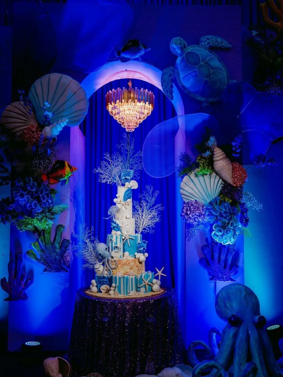Underwater themed party setup with a blue cake, coral, and sea creatures.