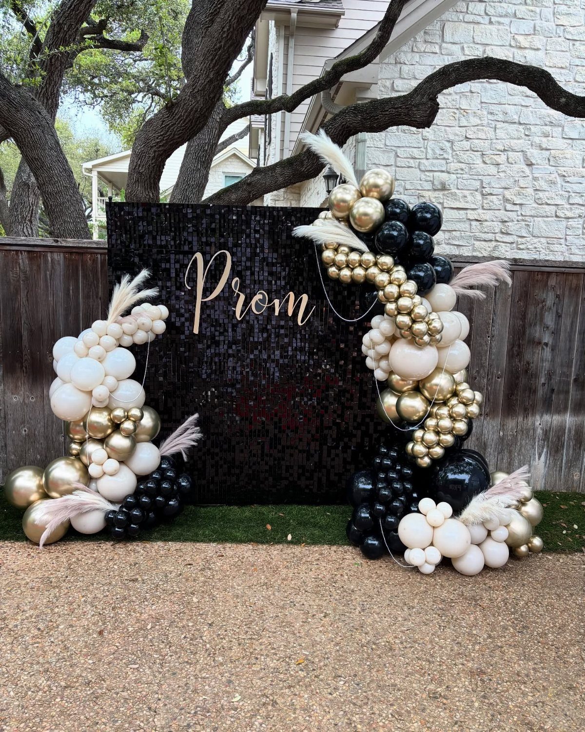 Black sequin prom backdrop with gold lettering and black, gold, and white balloons.