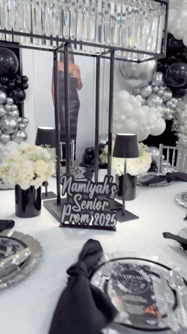 Prom table setting with white flowers, black sign, and silver plates with balloons.