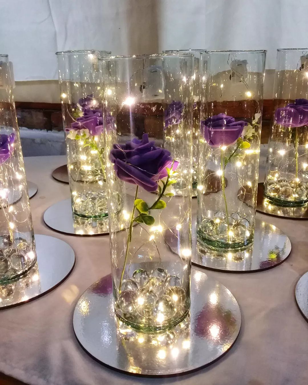 Purple roses in glass cylinder vases with fairy lights on mirror bases