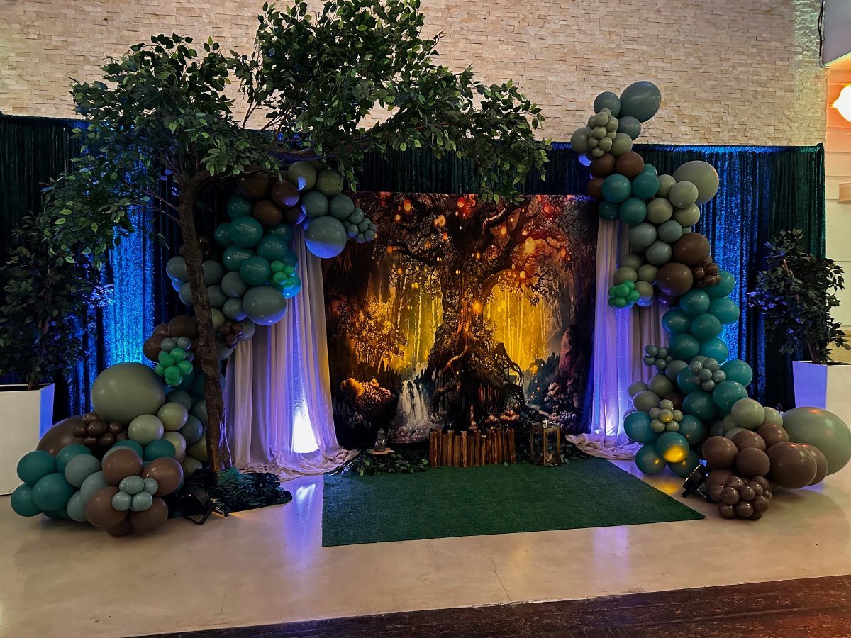 Forest themed event backdrop with green balloon arches and a printed woodland scene.