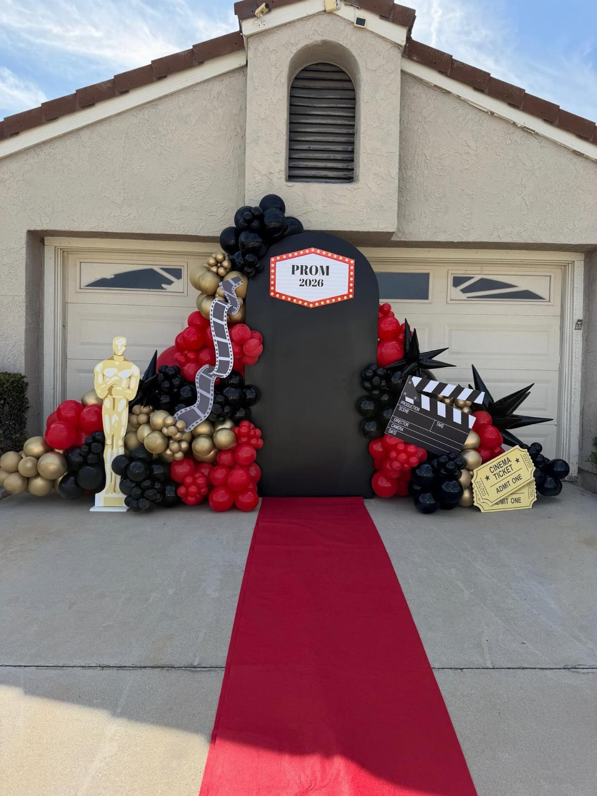 Red carpet entrance with gold statuette, movie clapperboard, and red and black balloons.