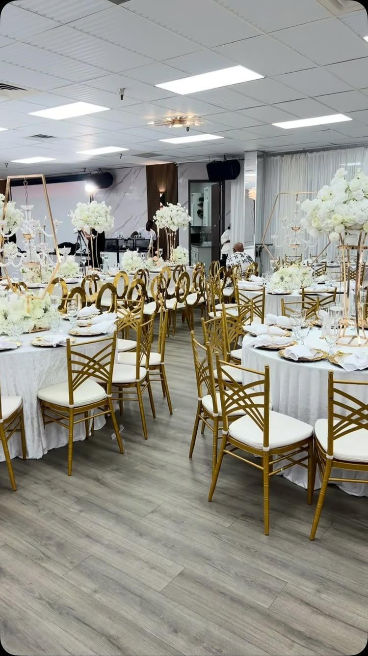 White floral centerpieces on gold stands atop white banquet tables with gold chairs.