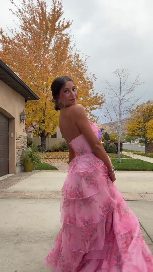 Young woman wearing a tiered pink floral prom dress posing on a driveway.