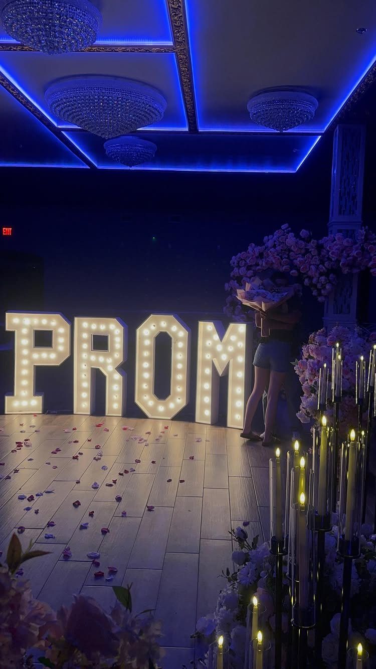 Large illuminated PROM marquee letters on a wooden floor with blue lighting.