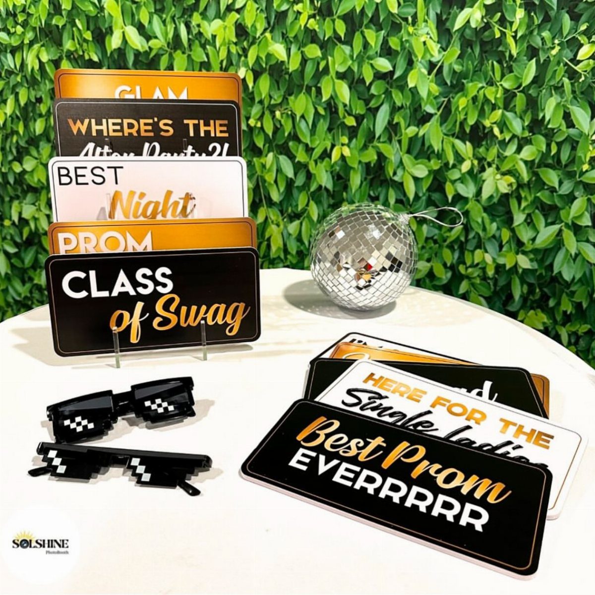 Prom photo booth props including themed signs, pixel glasses, and a disco ball.