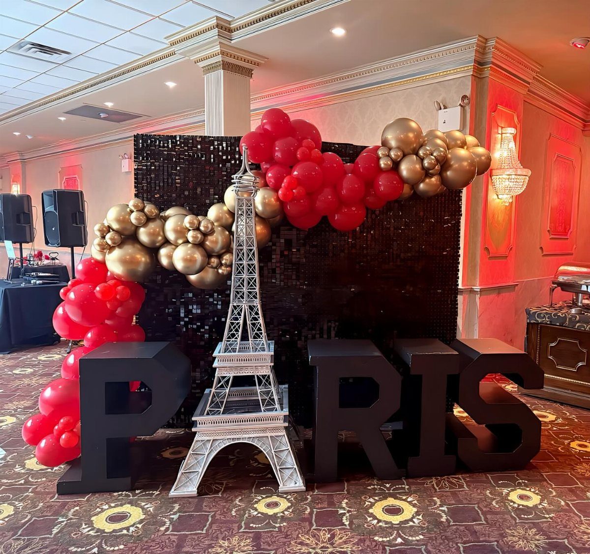 Eiffel Tower model and PARIS letters with red and gold balloons against sequin backdrop