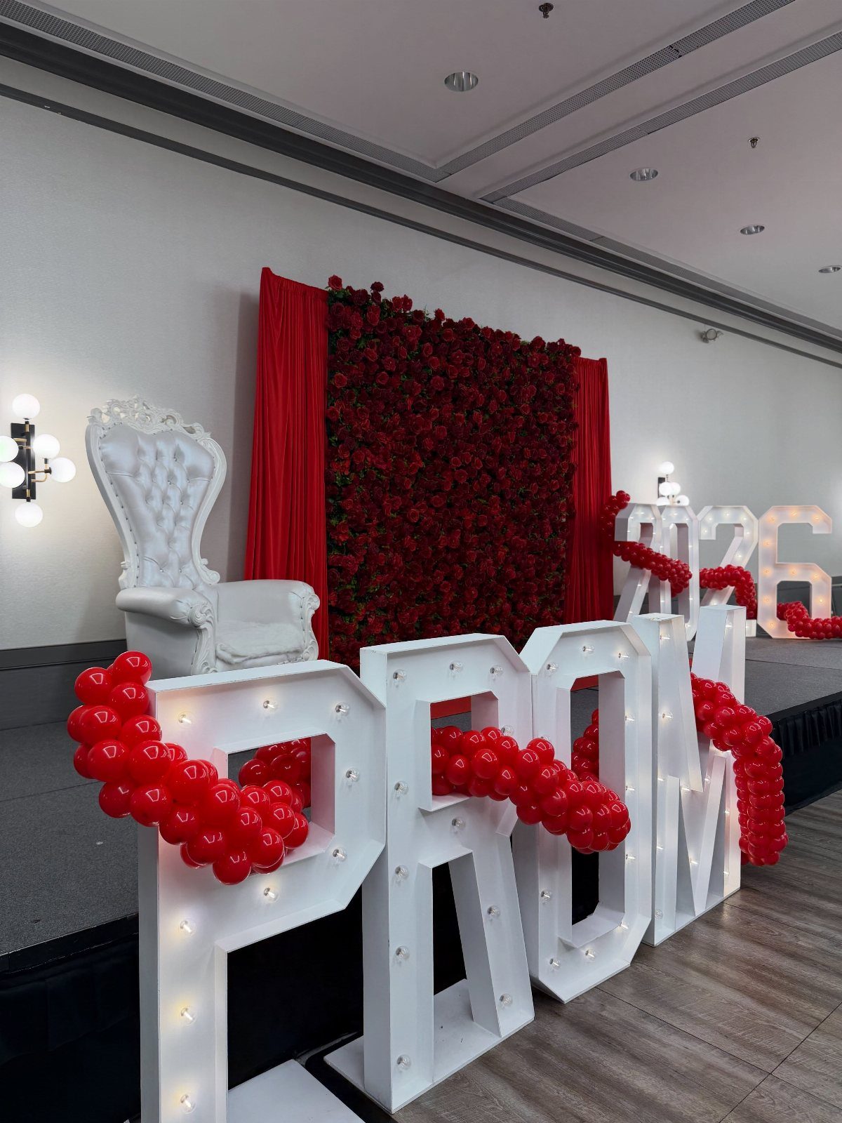 Large illuminated PROM letters with red balloons and a red rose wall backdrop.