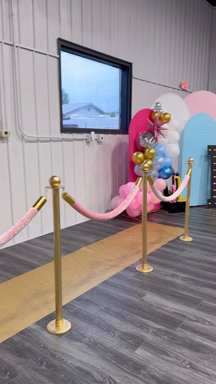 Gold carpet runner with pink velvet ropes and colorful balloon decorations in a room.