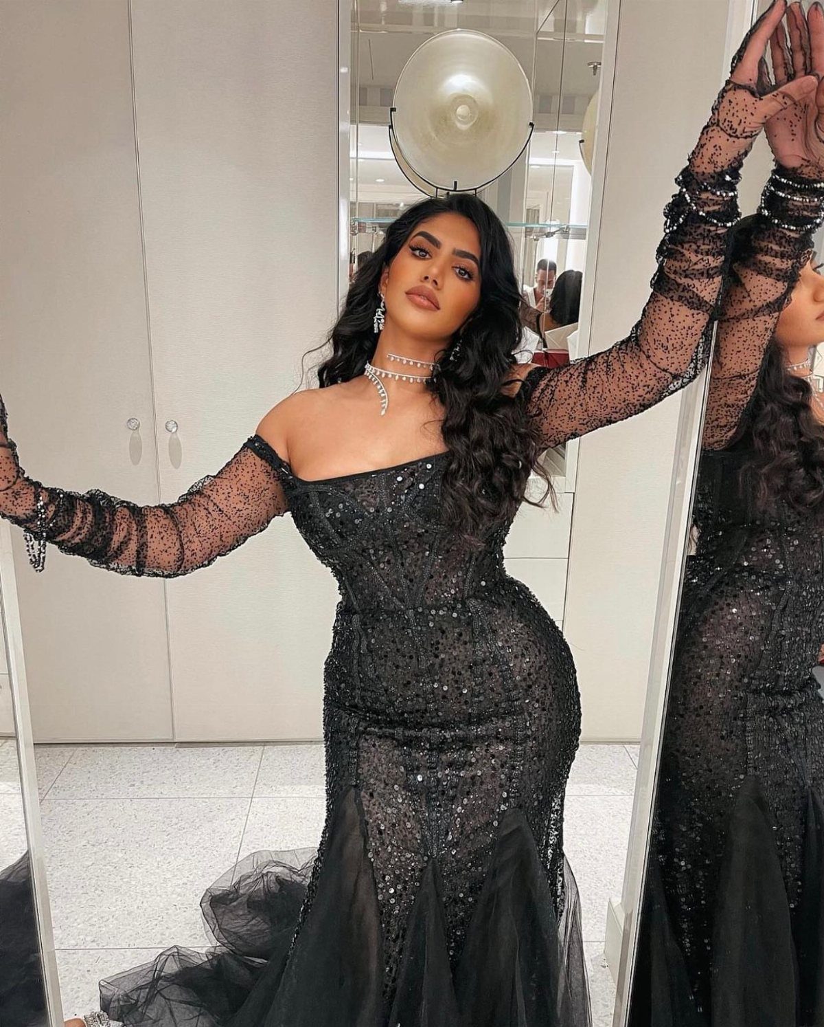 Woman in a sparkling black off-the-shoulder gown posing in a bright room.