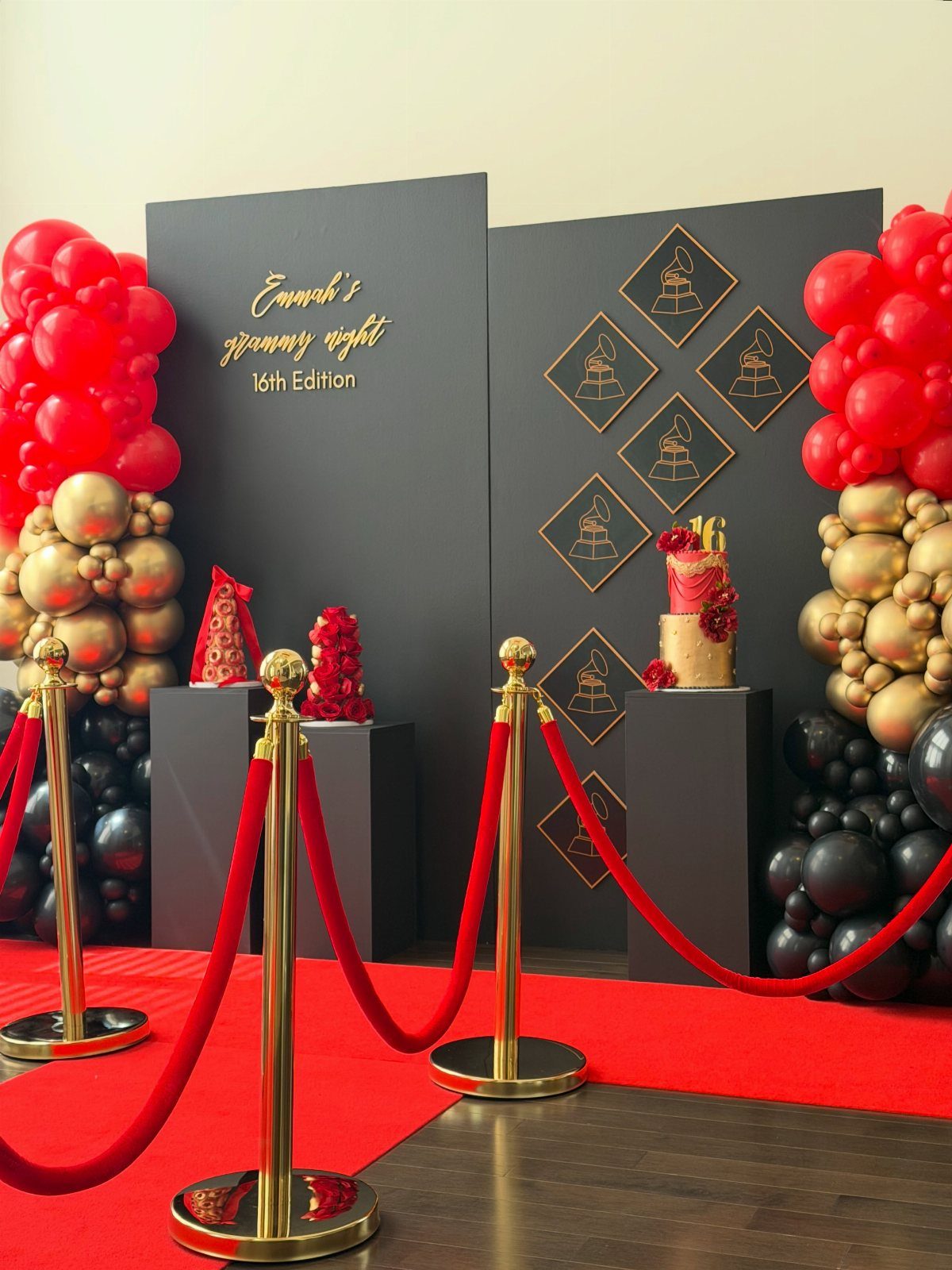 Black step-and-repeat backdrop with gold accents, red carpet, and balloon arches.