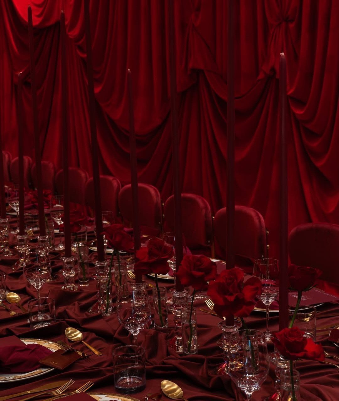 Red fabric tablecloth on a dining table with red roses and tall candles.