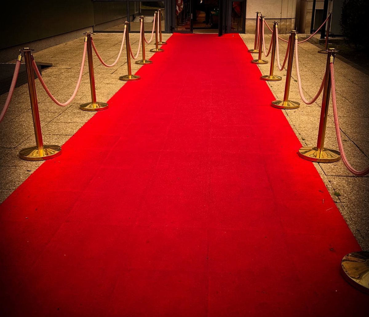 Red carpet leading to an entrance with gold stanchions and red velvet ropes.