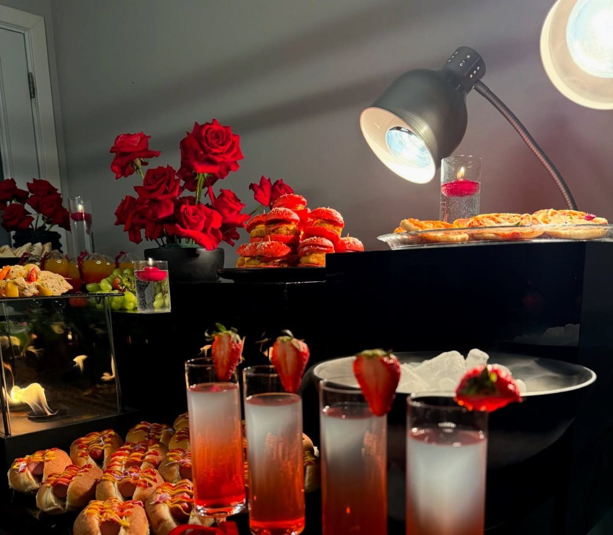 Red-bun sliders and strawberry-garnished cocktails arranged on a black table with red roses.