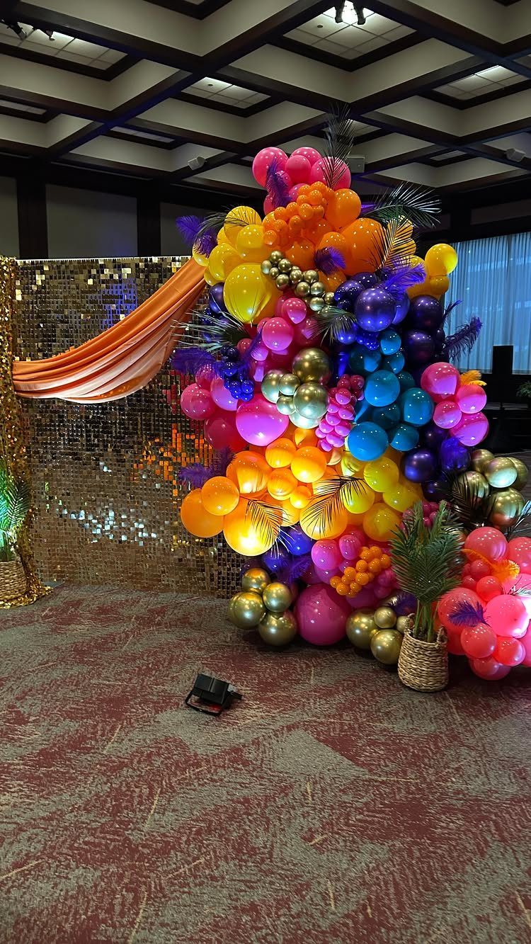 Colorful balloon installation with tropical leaves next to a gold sequin wall.