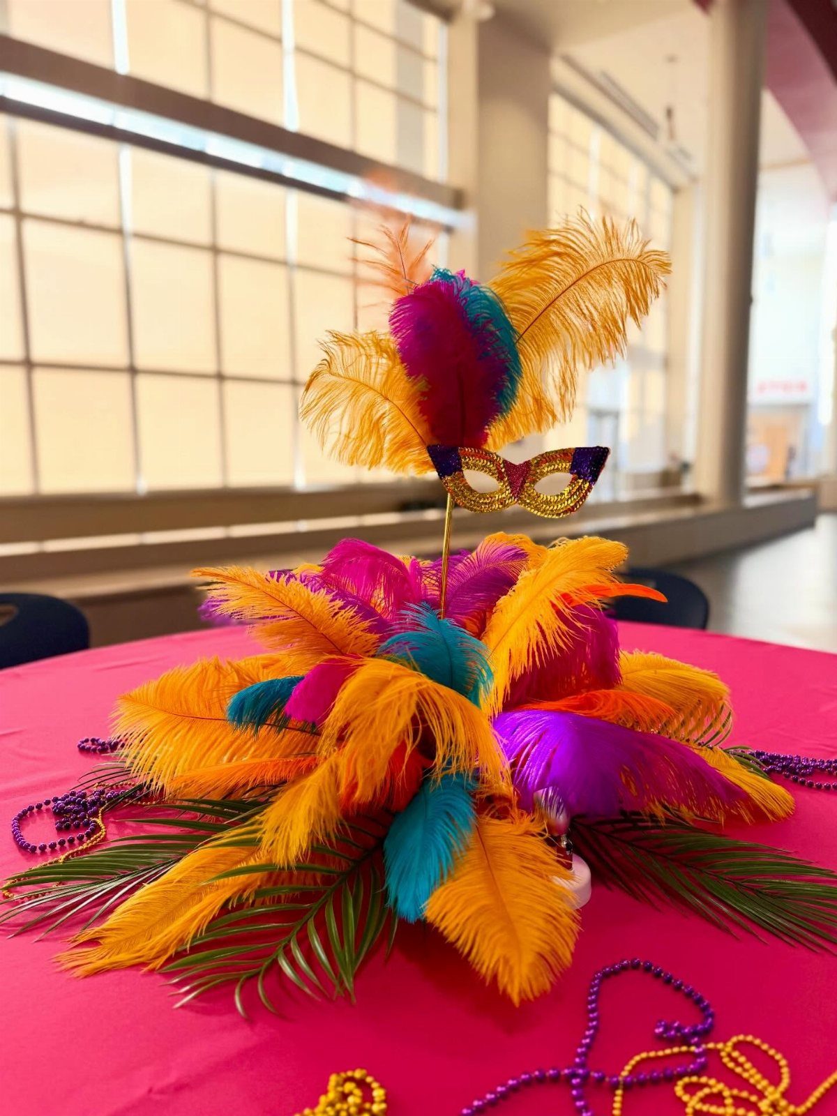 Vibrant ostrich feather centerpiece with a gold mask on a pink table.