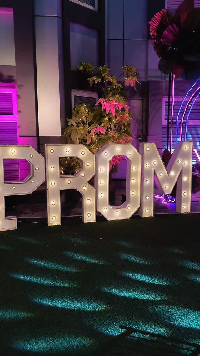 Large white marquee PROM letters with glowing bulbs and purple ambient lighting.