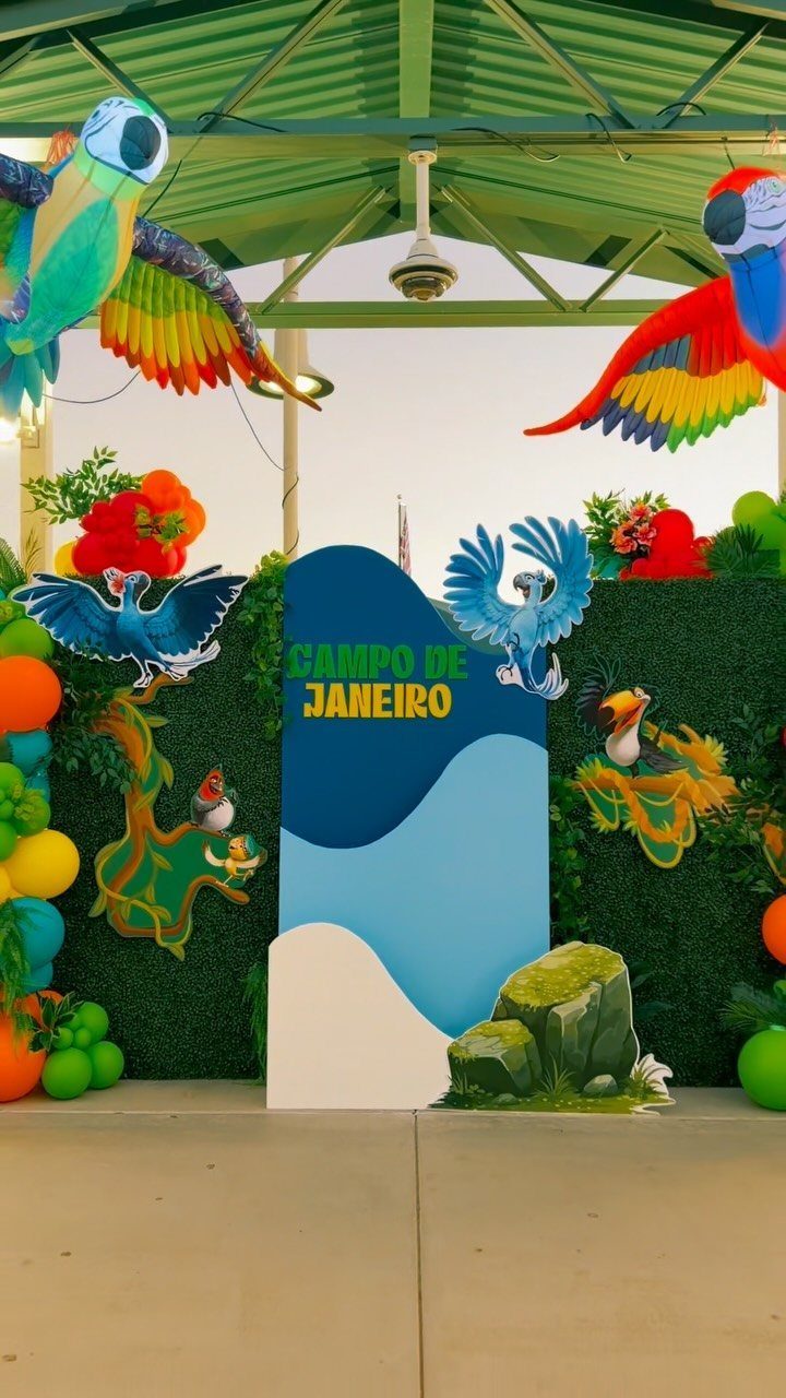 Tropical themed backdrop with colorful bird cutouts and a green hedge wall.