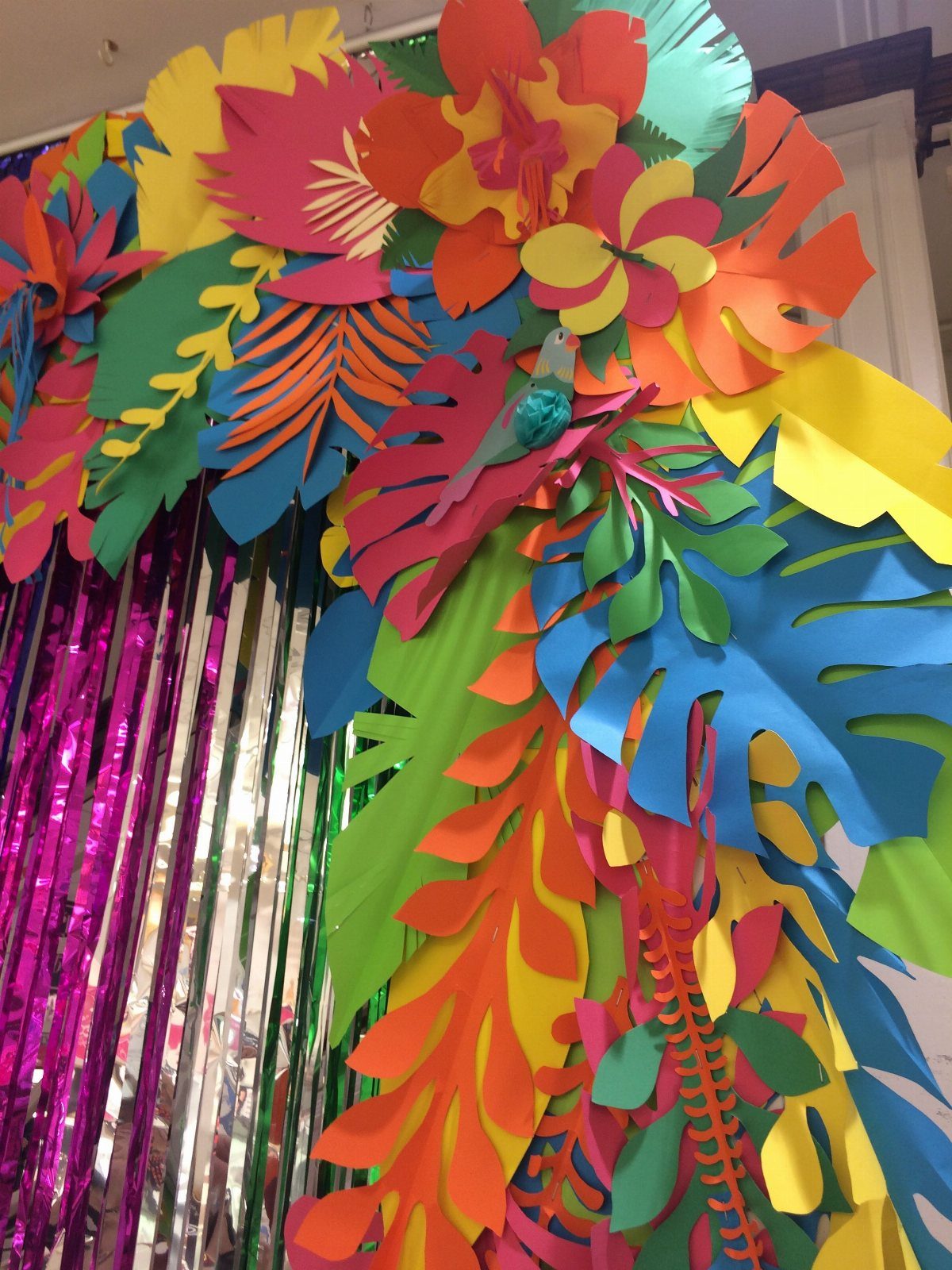 Tropical paper flower and leaf archway with a shimmering purple foil curtain.