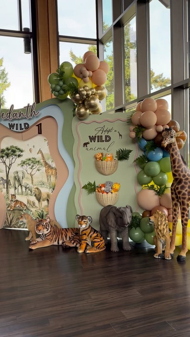 Safari party decoration with animal plushies, earth-toned balloons, and a themed backdrop.