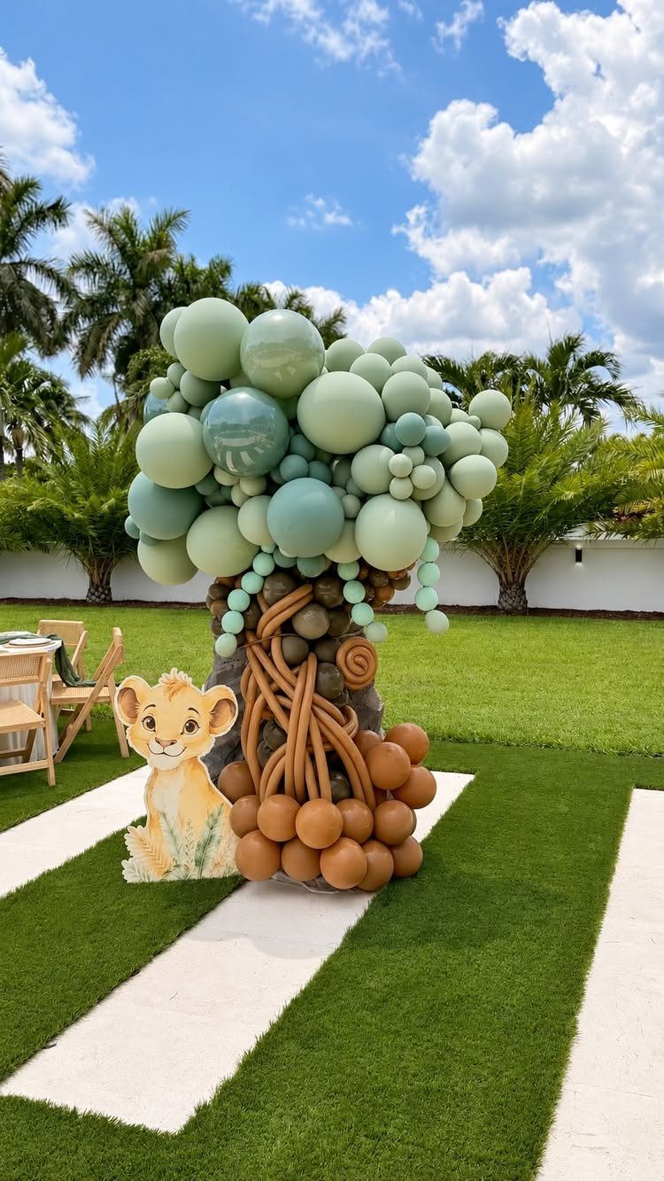 Balloon tree sculpture and lion cub cutout on a lawn for a safari party.