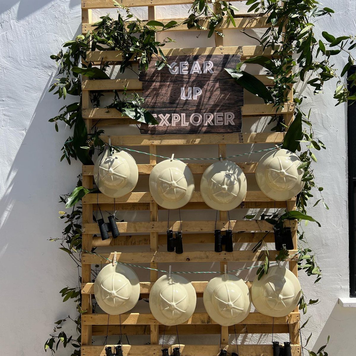 Wooden pallet wall with pith helmets and binoculars for a safari party