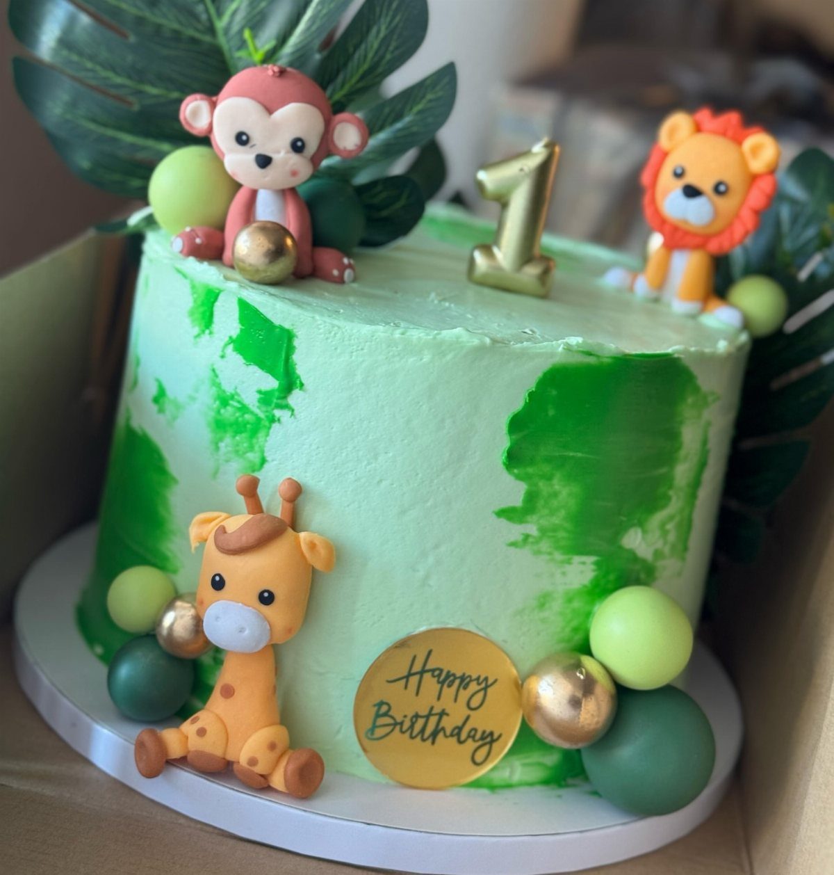 Safari themed birthday cake with animal figures, green frosting, and tropical leaves.