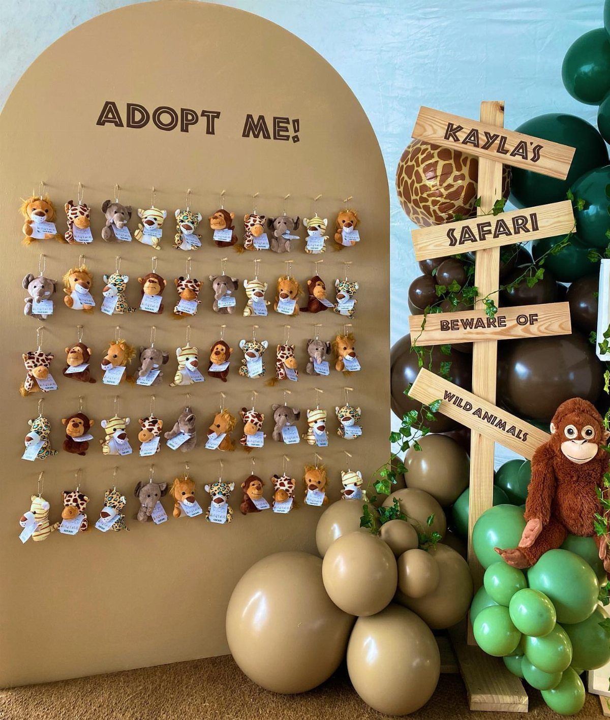 Plush safari animals hanging on a tan backdrop for a party favor station.