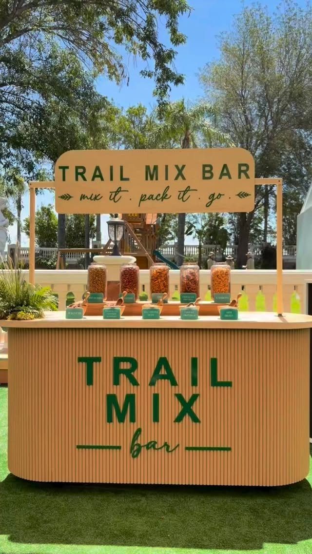 Trail mix bar with glass dispensers of snacks on a wooden outdoor counter.