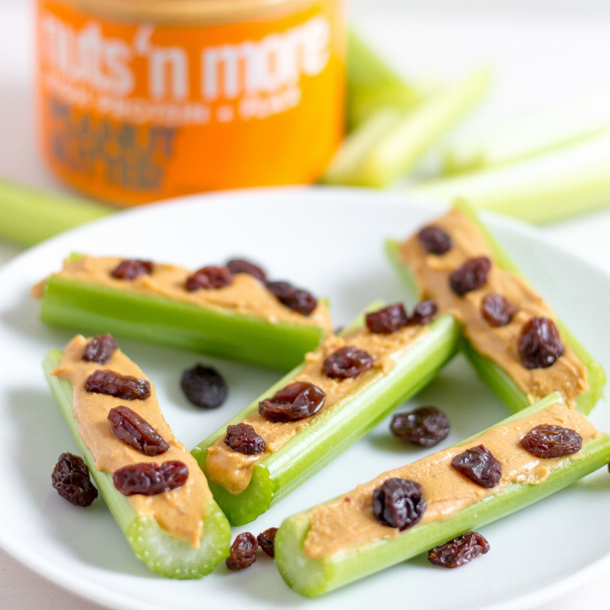 Celery sticks filled with peanut butter and topped with raisins on a white plate.