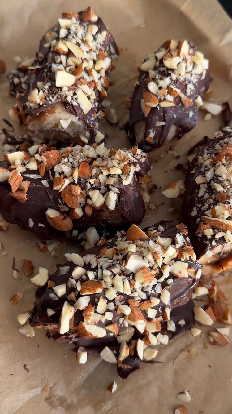 Chocolate covered banana slices topped with crushed almonds on brown parchment paper.