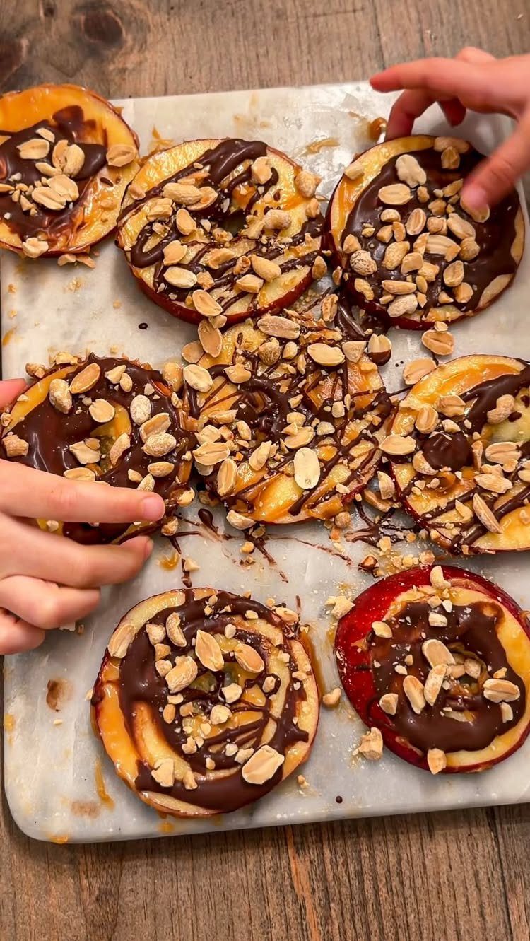 Apple slices topped with melted chocolate and peanuts on a baking sheet.