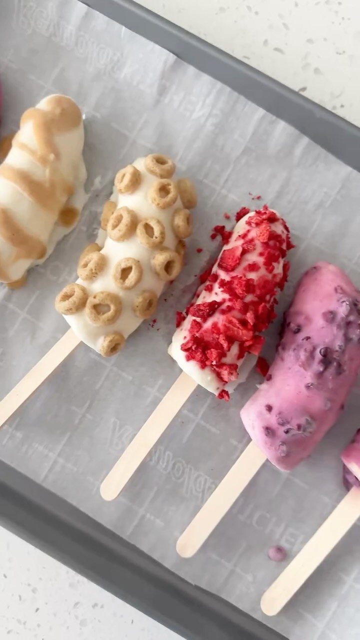 Frozen banana pops coated in colorful yogurt and topped with various crunchy toppings.