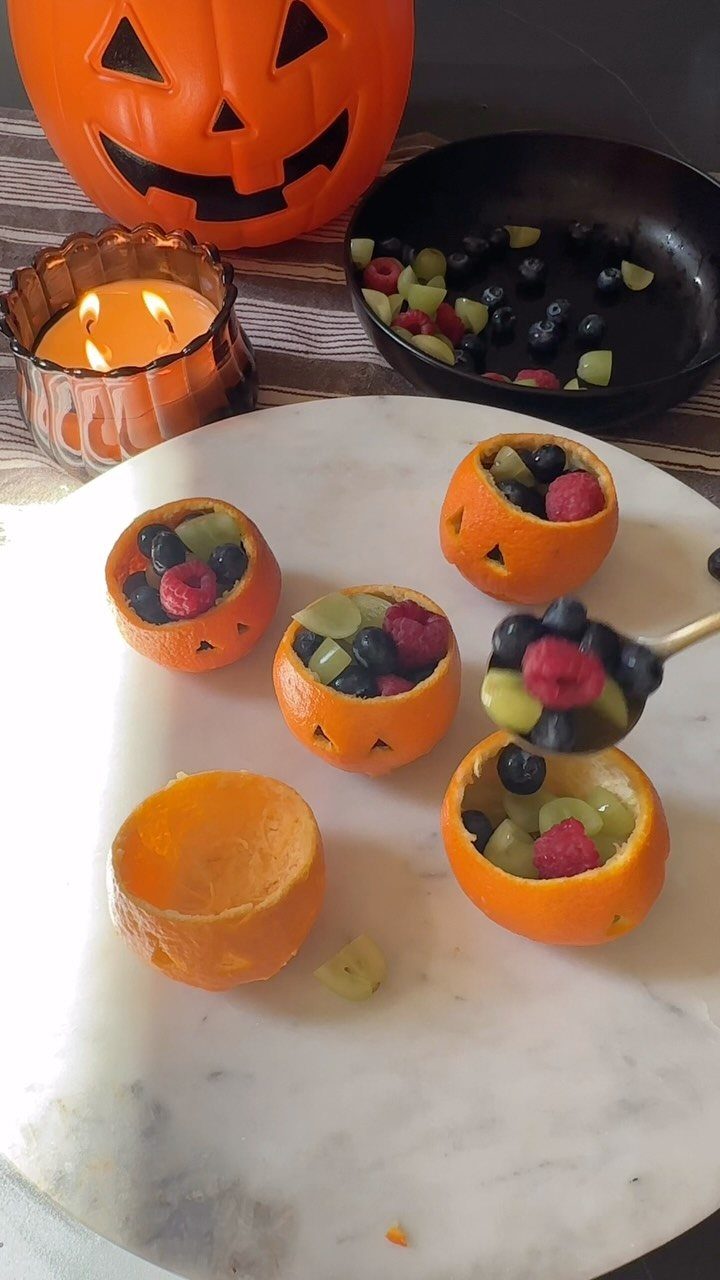 Orange peel jack-o'-lanterns filled with mixed berries and grapes on marble surface