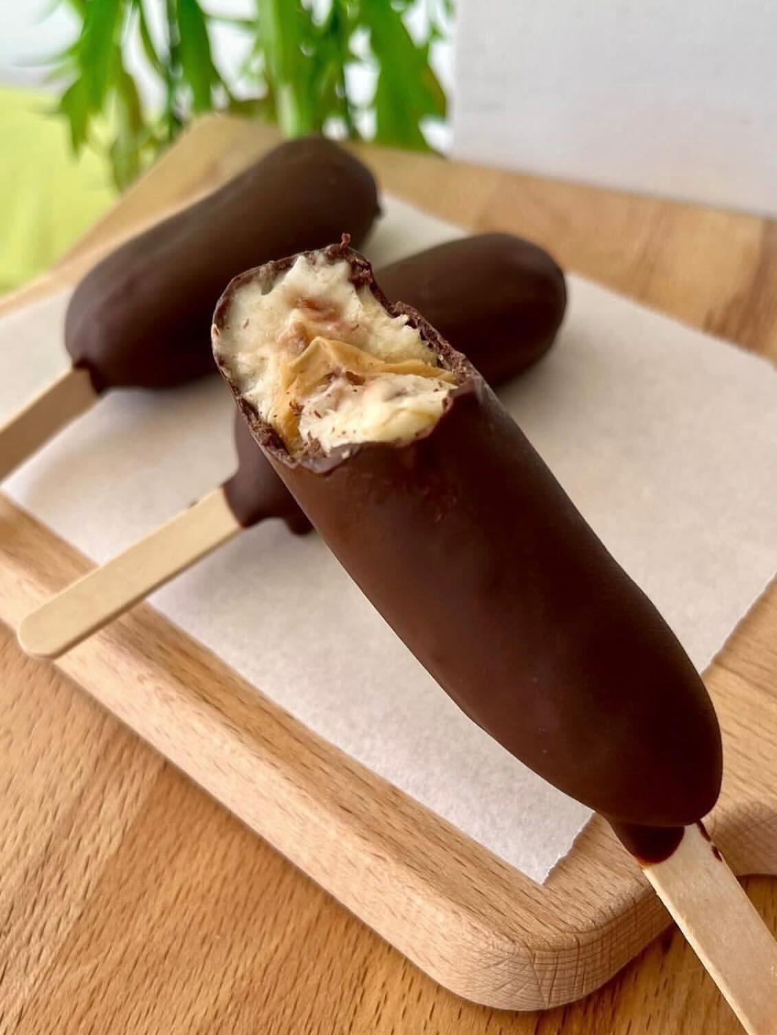 Chocolate-covered peanut butter popsicles on wooden sticks resting on a wooden board.
