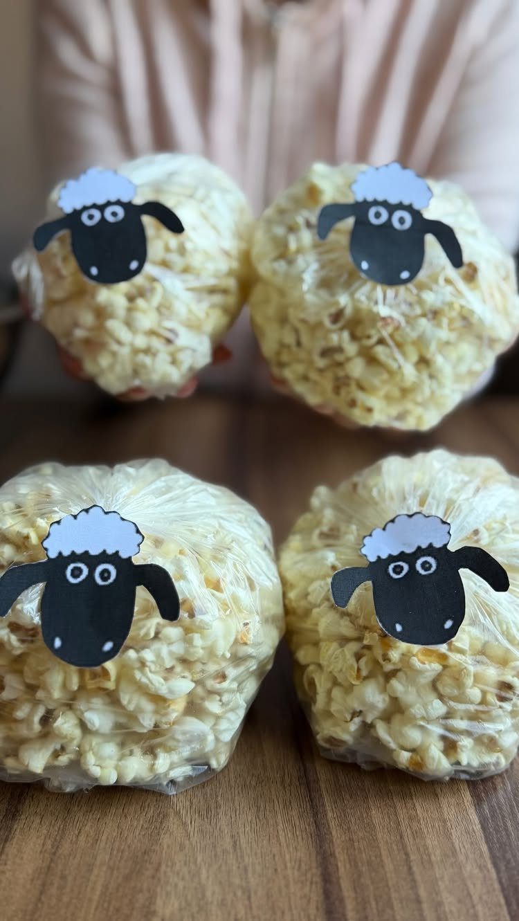 Popcorn in clear bags decorated with cute paper sheep faces on wooden table