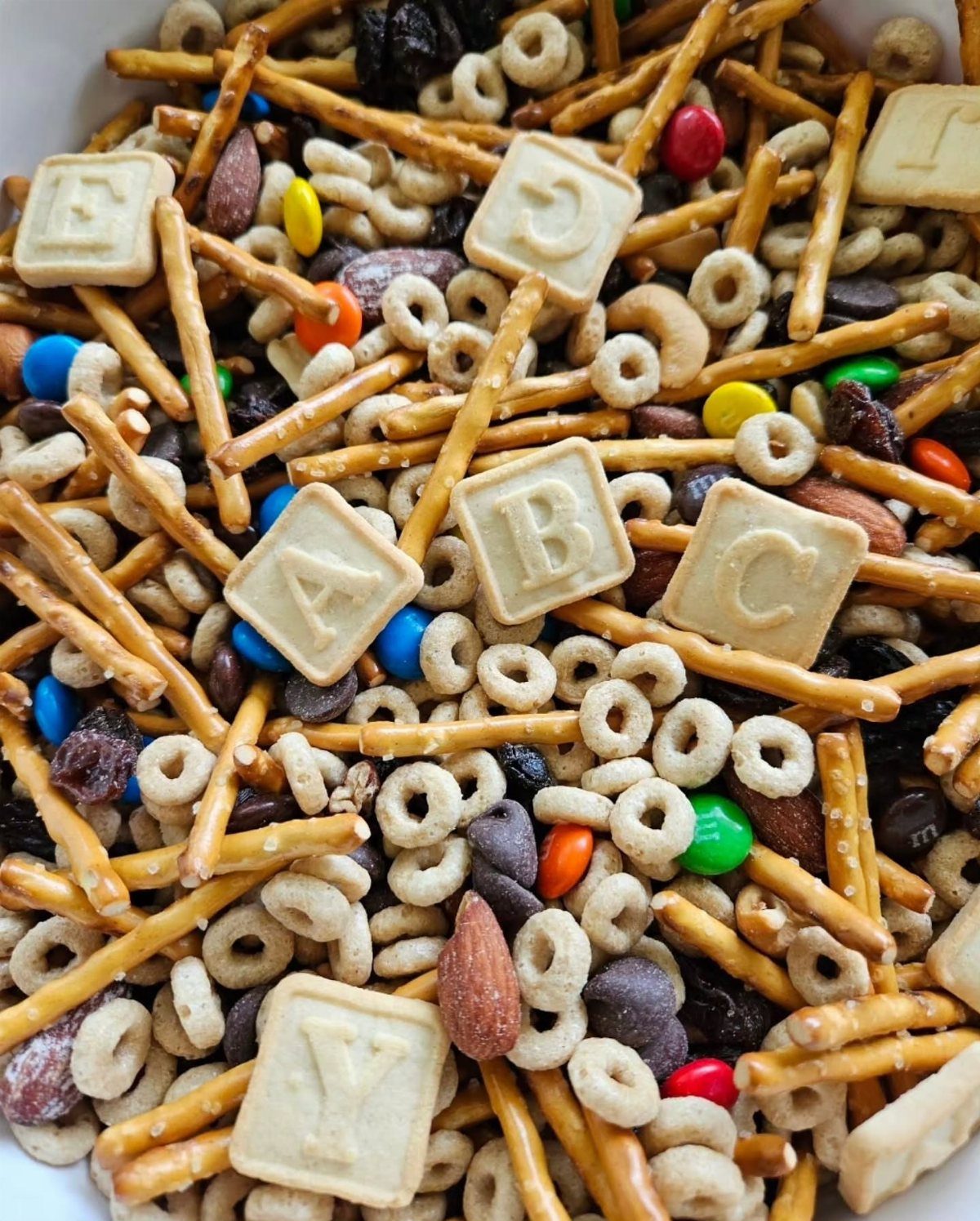 Trail mix with pretzel sticks, alphabet crackers, cereal, nuts, and colorful candies.