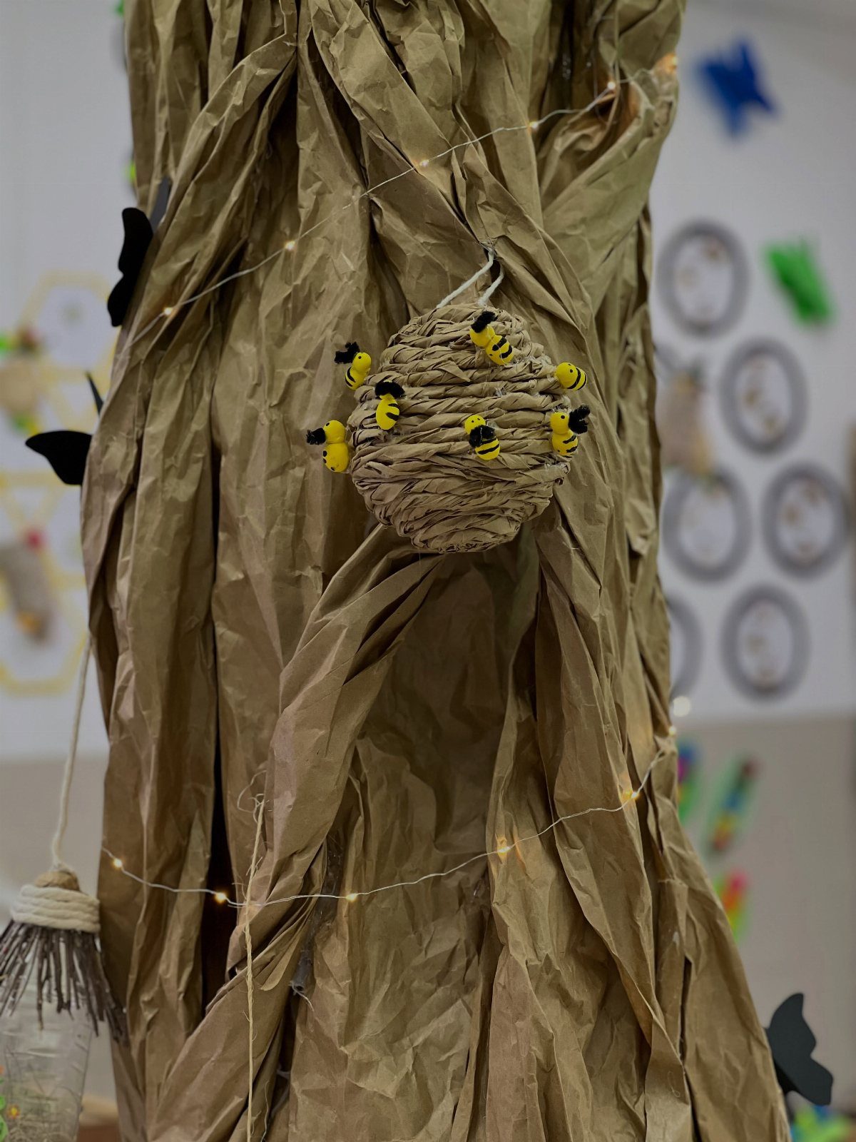 Brown paper tree trunk with a beehive and small bees in a classroom.
