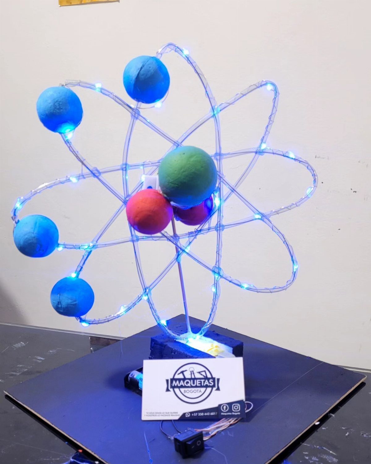 Atom model with colorful spheres and blue LED lights on a black base.