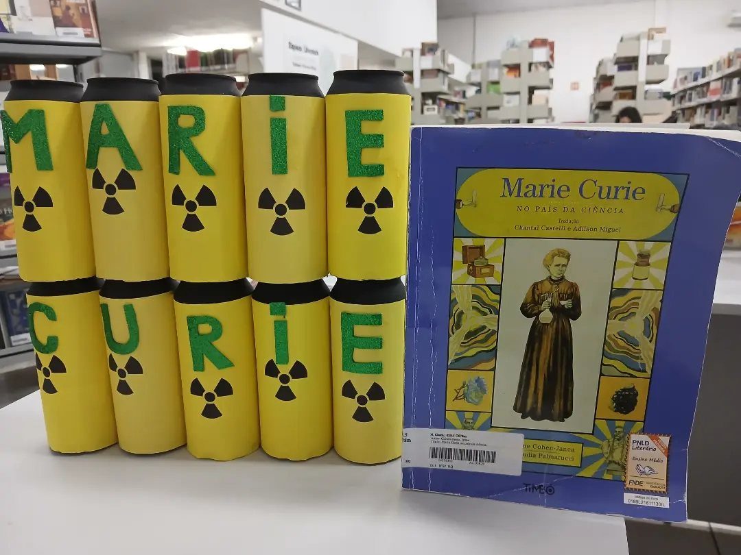 Yellow cylinders spelling Marie Curie with radiation symbols next to a biography book.