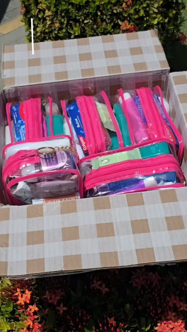 Checkered box filled with pink-trimmed clear pouches containing various personal care items.