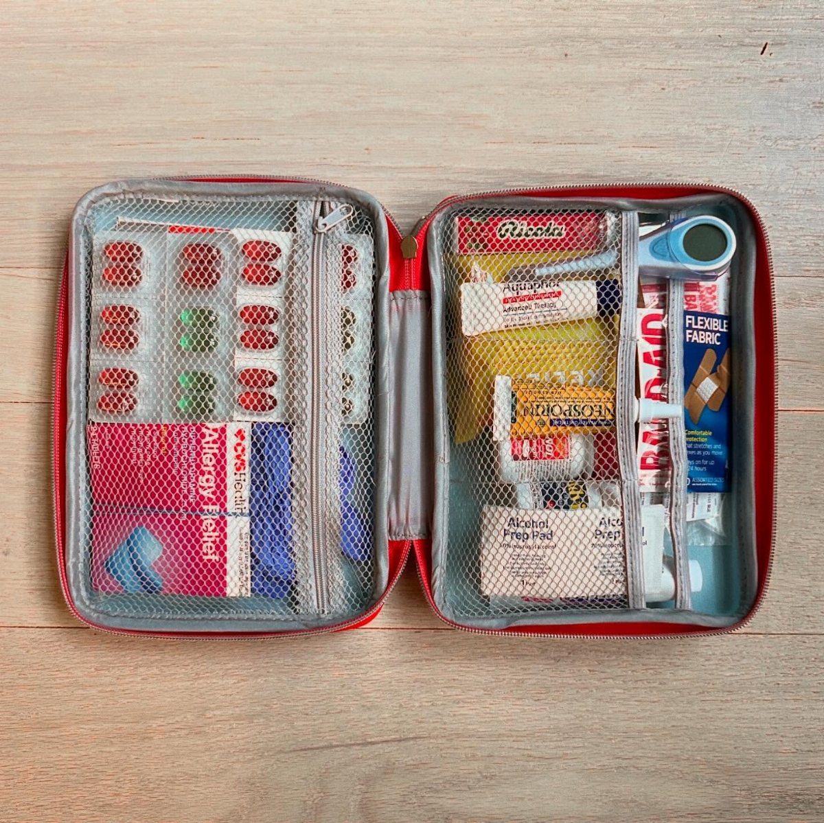 Open red first aid kit containing medical supplies and Ricola cough drops on wood.