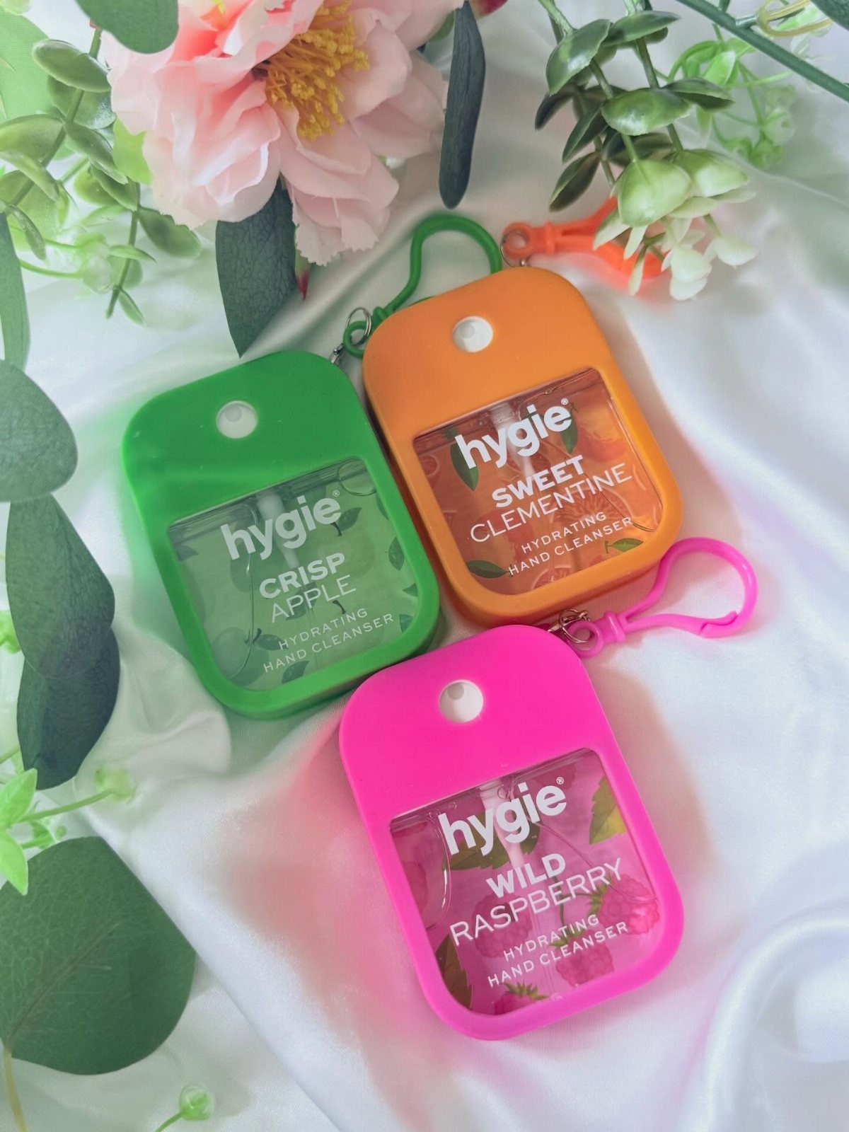 Three colorful Hygie hand cleanser containers with clips on white fabric with flowers.